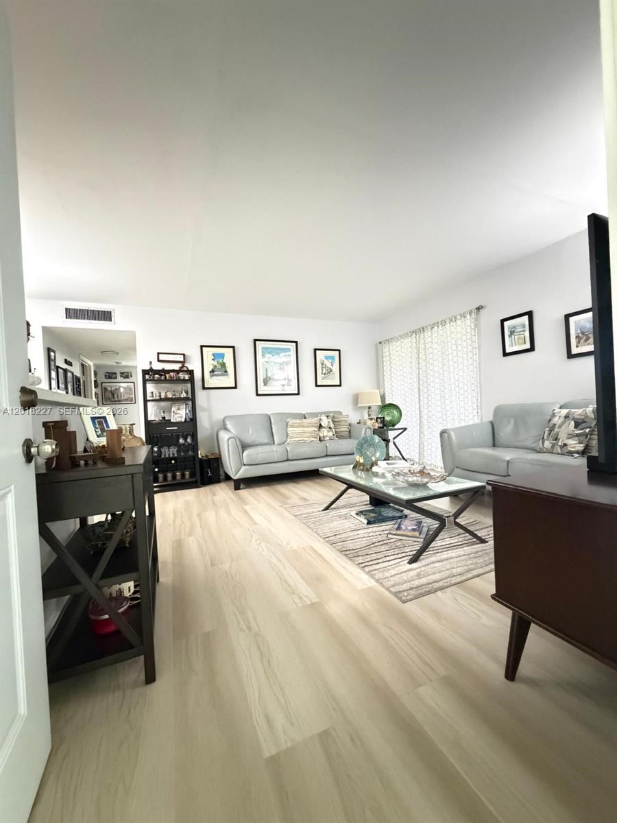 A living room features light wood-look flooring, two light gray sofas, and a glass coffee table — 761 NE 199th St # 102, Miami FL 33179, MIAMI, FL