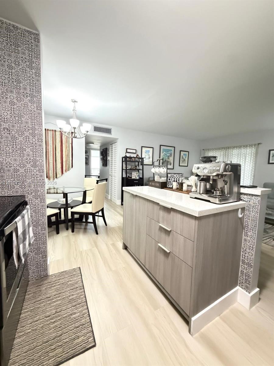 A kitchen island with a coffee machine sits in front of a dining area — 761 NE 199th St # 102, Miami FL 33179, MIAMI, FL
