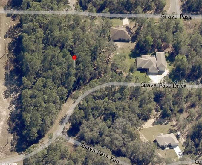 This aerial view shows a wooded lot marked with a red pin near residential streets — Lot 26 GUAVA PASS DRIVE, OCKLAWAHA, FL