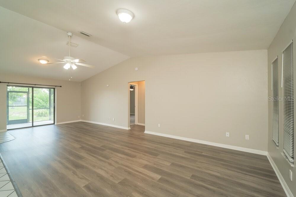 An empty living room with vaulted ceilings, light-colored walls, and wood-look flooring — 1329 SE 12TH STREET, CAPE CORAL, FL