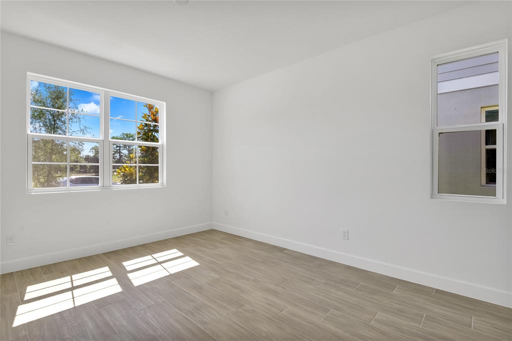 An empty room with white walls, light wood-look tile flooring, and two windows — 141 WATERSTONE LOOP, TAVARES, FL