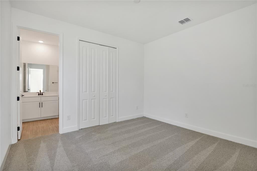 A bedroom with gray carpet, white walls, a closet, and an attached bathroom — 141 WATERSTONE LOOP, TAVARES, FL