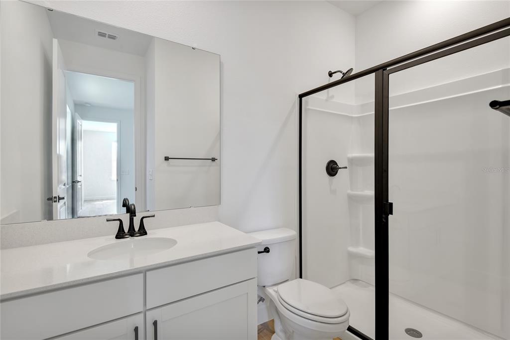 A bathroom features a white vanity, a black faucet, a toilet, and a glass-enclosed shower — 141 WATERSTONE LOOP, TAVARES, FL