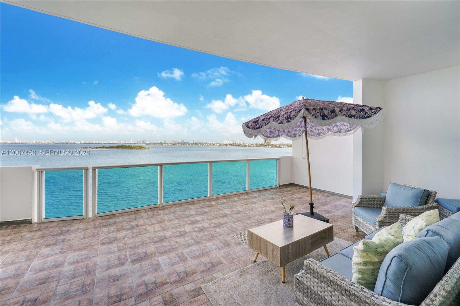 A balcony with tiled flooring, outdoor furniture, and a patterned umbrella overlooks the ocean — 725 NE 22nd St # 7B, Miami FL 33137, MIAMI, FL