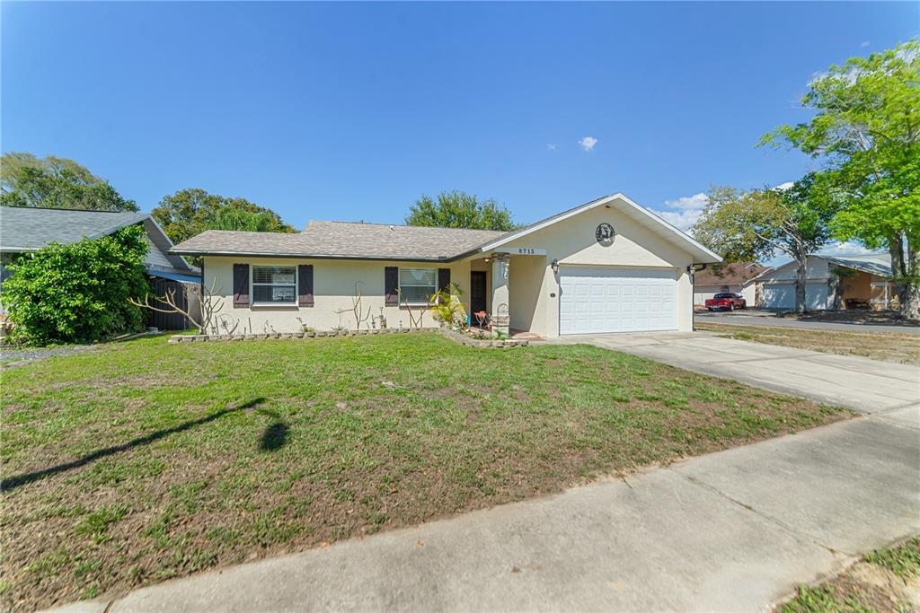 A single-story house with a beige stucco exterior, a two-car garage, and a front lawn — 8715 HUNTSMAN LANE, PORT RICHEY, FL