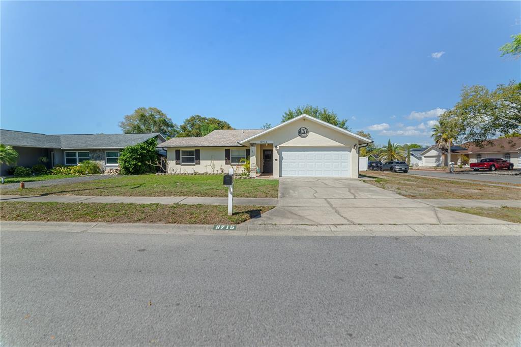 A single-story house with a white garage, beige siding, and a front lawn — 8715 HUNTSMAN LANE, PORT RICHEY, FL