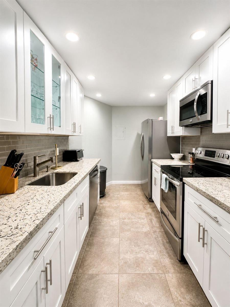 A galley kitchen features white cabinets, granite countertops, stainless steel appliances, and a tiled backsplash — 1200 Hibiscus Avenue # 806, Pompano Beach FL 33062, POMPANO BEACH, FL