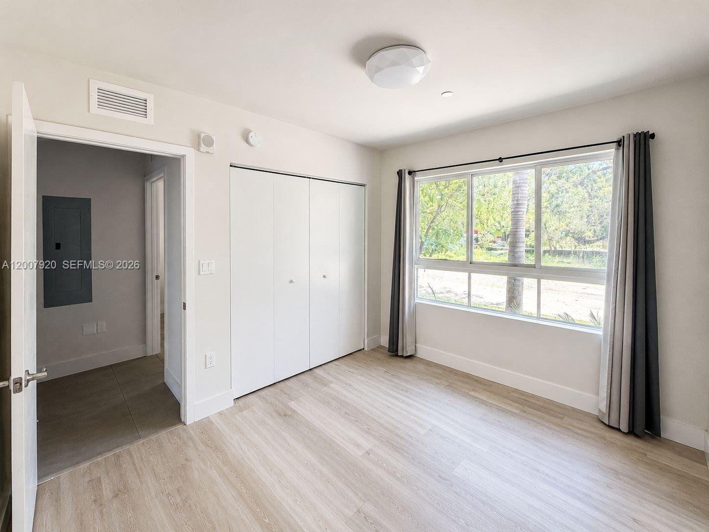 A bedroom features light wood-look flooring, a white closet, and a window with curtains — 2505 NE 193rd St # 4112, Miami FL 33180, MIAMI, FL