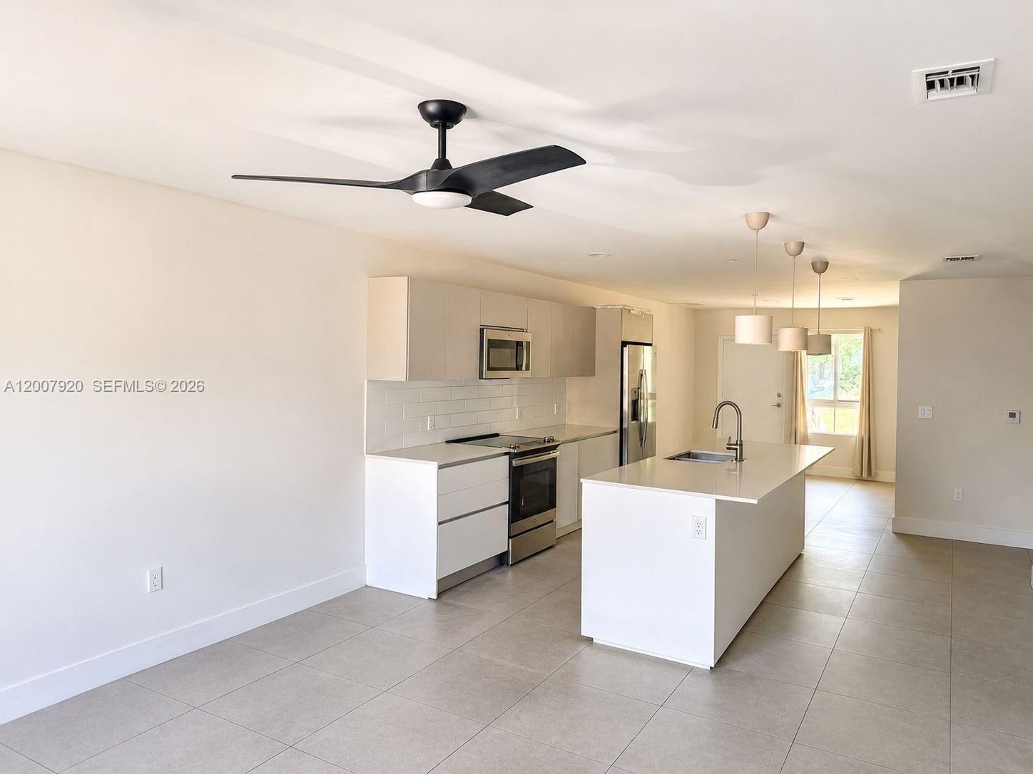 A modern kitchen features white cabinetry, a central island, stainless steel appliances, and tile flooring — 2505 NE 193rd St # 4112, Miami FL 33180, MIAMI, FL