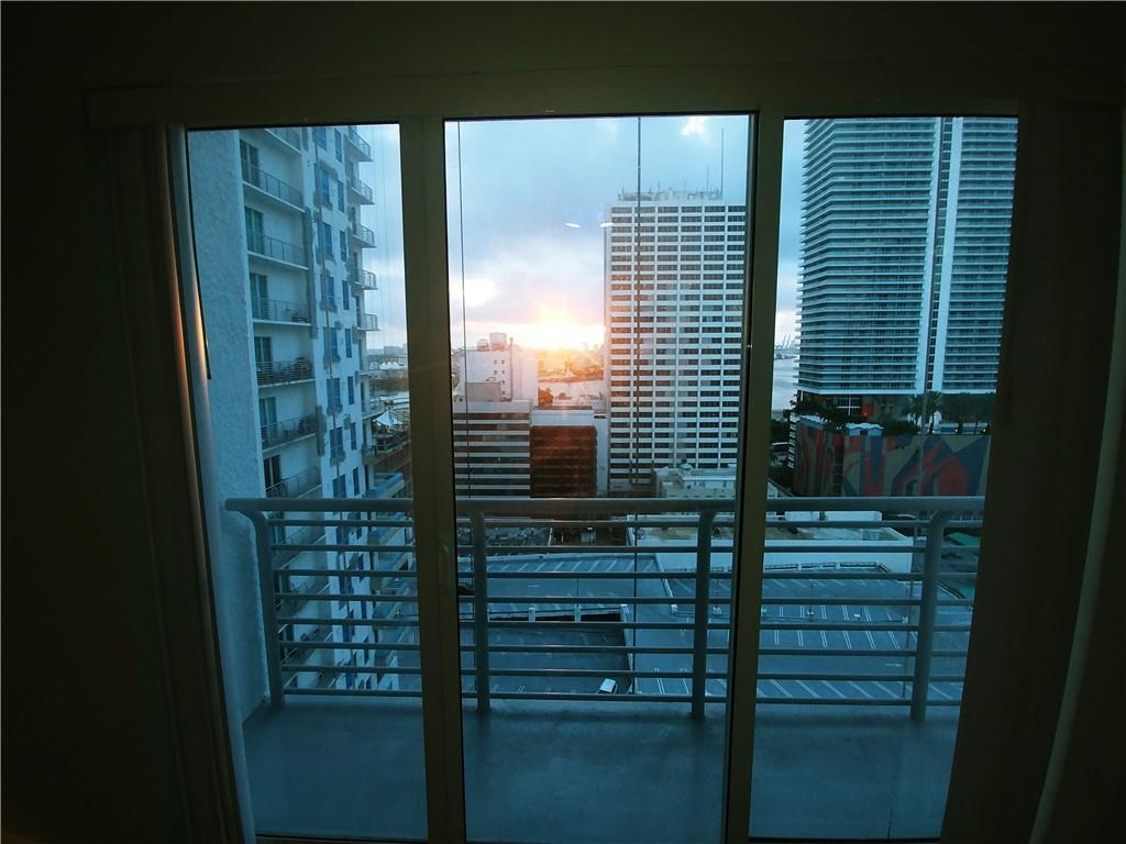 A view of city skyscrapers and a parking lot from a balcony through glass doors — 133 NE 2nd Avenue # 1812, Miami FL 33132, MIAMI, FL