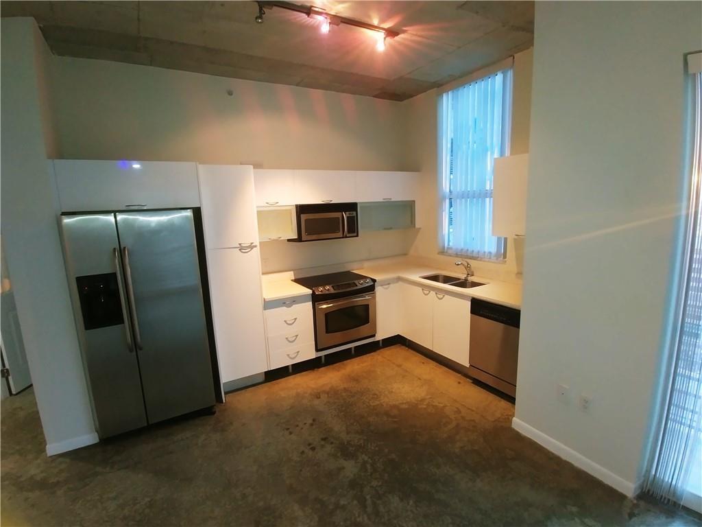 A modern kitchen features stainless steel appliances, white cabinetry, and exposed concrete floors and ceilings — 133 NE 2nd Avenue # 1812, Miami FL 33132, MIAMI, FL