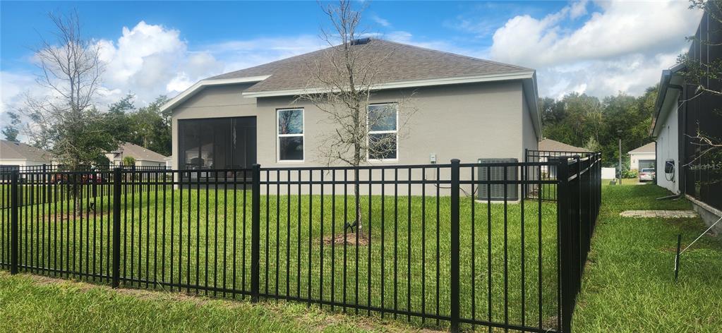 A fenced backyard features a gray house with a screened-in porch and an air conditioning unit — 9032 CAPE COD ROAD, DELAND, FL