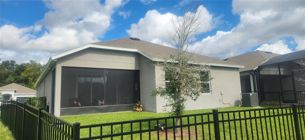 The exterior rear view of a house features a screened-in patio and a black metal fence — 9032 CAPE COD ROAD, DELAND, FL