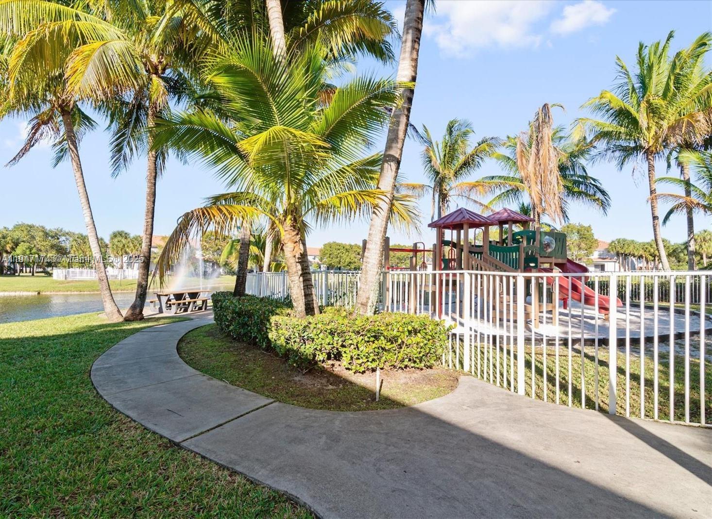 A concrete path leads past a fenced playground and palm trees toward a small lake — 8208 SW 25th Ct # 103, Miramar FL 33025, MIRAMAR, FL