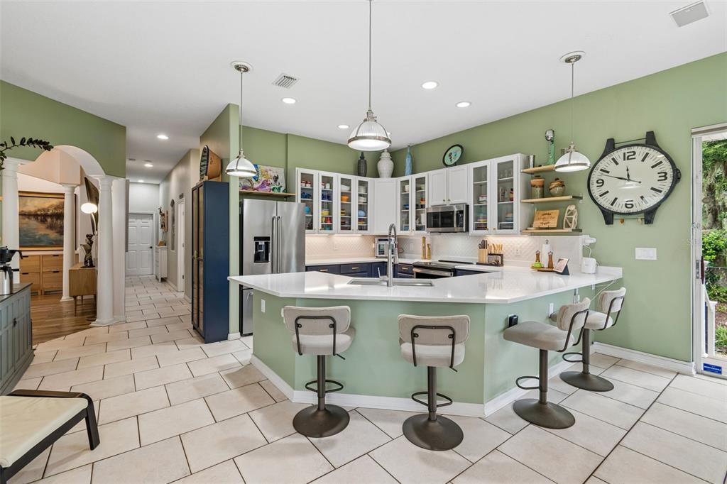 A kitchen features light green walls, white cabinets, a quartz-topped peninsula, and three bar stools — 1514 BOOTH DRIVE, VALRICO, FL