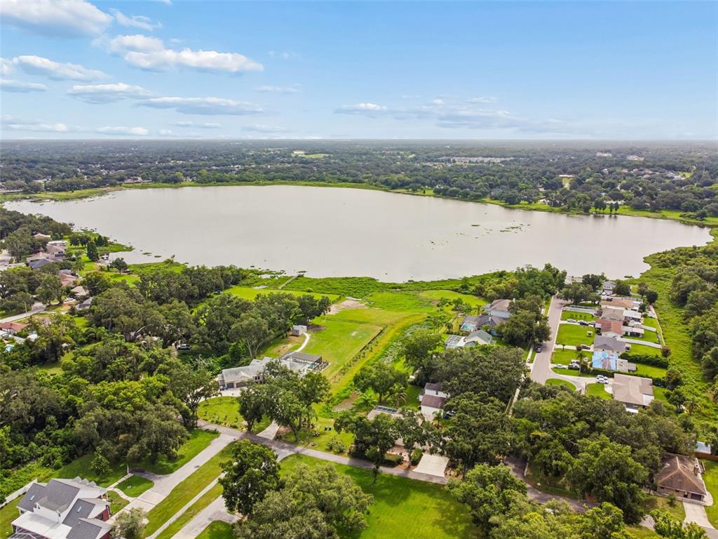 An aerial view shows a large lake surrounded by residential houses and dense green trees — 1514 BOOTH DRIVE, VALRICO, FL