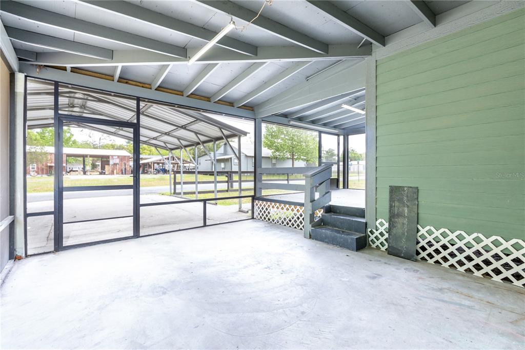 A covered concrete patio features a screened enclosure, wooden steps, and green exterior siding — 408 S ORANGE STREET, STARKE, FL