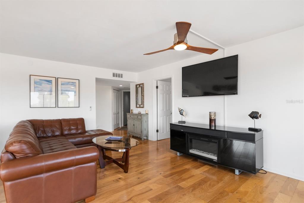 A living room features a brown leather sectional, hardwood floors, a ceiling fan, and television — 6269 PALMA DEL MAR BOULEVARD S UNIT 302, ST PETERSBURG, FL