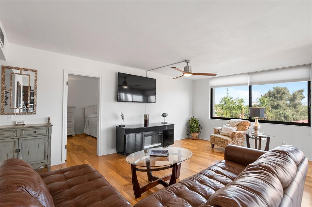 A living room features a brown leather sofa, wood flooring, a television, and large windows — 6269 PALMA DEL MAR BOULEVARD S UNIT 302, ST PETERSBURG, FL