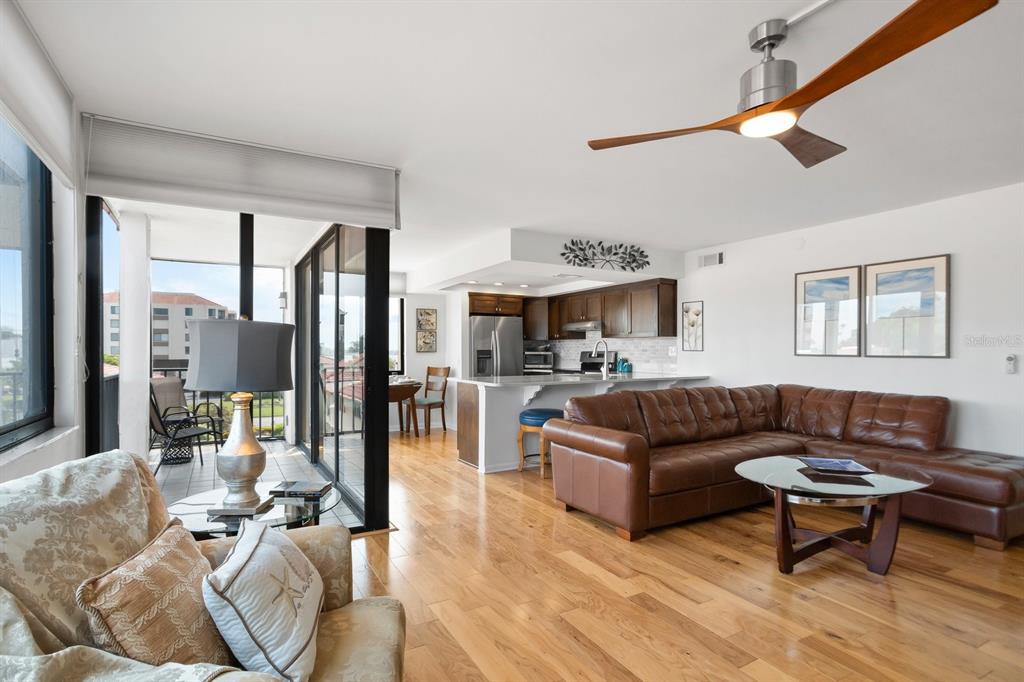 An open-concept living room and kitchen featuring hardwood floors, a brown leather sectional, and balcony — 6269 PALMA DEL MAR BOULEVARD S UNIT 302, ST PETERSBURG, FL