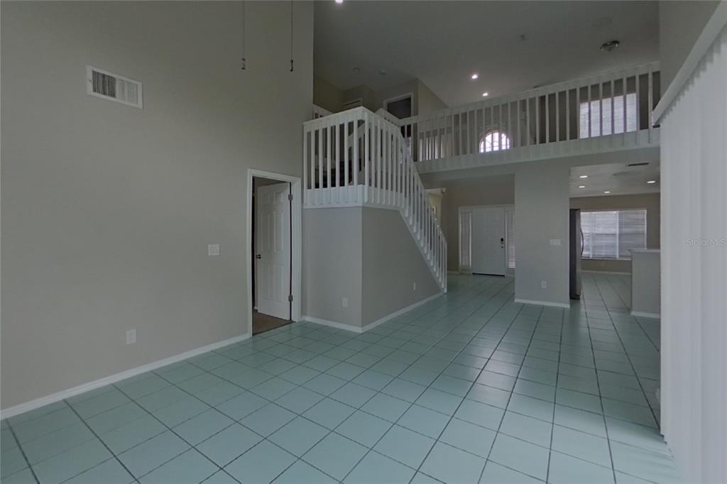 A high-ceilinged room features light-colored tile flooring, a white staircase, and an upper-level balcony — 3257 BREWSTER DRIVE, KISSIMMEE, FL