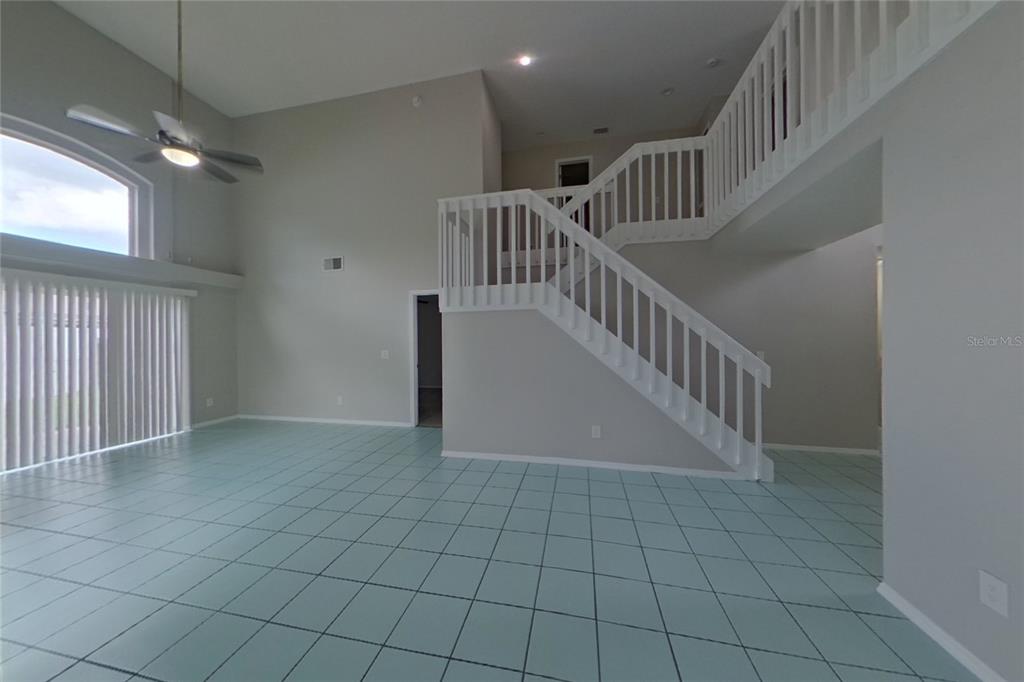 A spacious living area features light blue tile flooring, a high ceiling, and a staircase — 3257 BREWSTER DRIVE, KISSIMMEE, FL