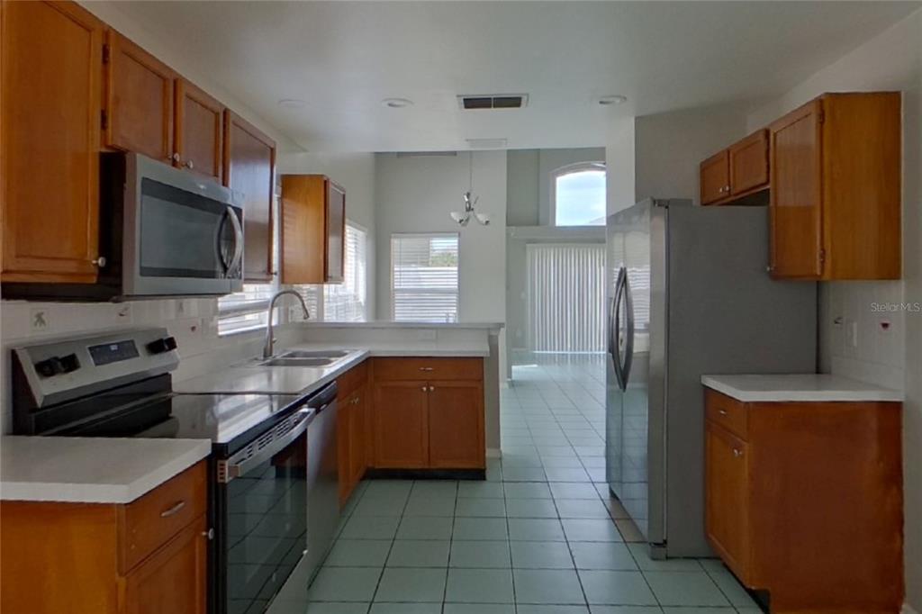 A kitchen with wood cabinets, stainless steel appliances, white countertops, and light-colored tile flooring — 3257 BREWSTER DRIVE, KISSIMMEE, FL