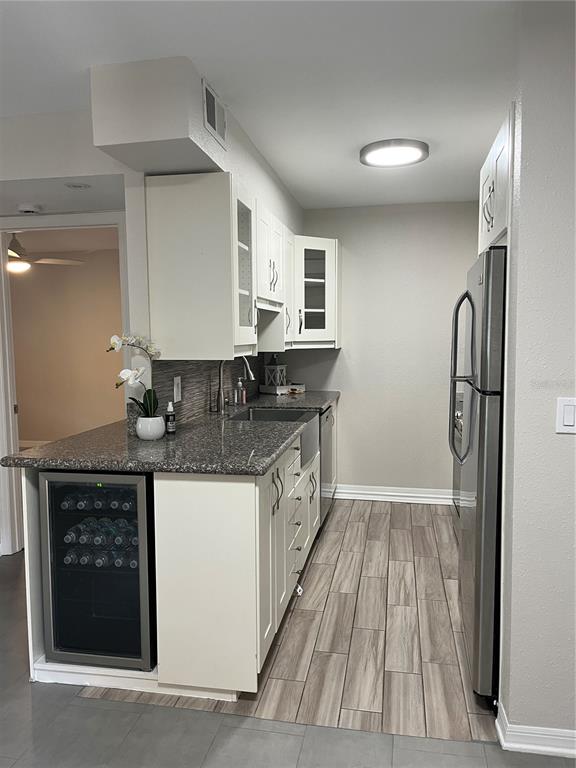 A kitchen features white cabinets, granite countertops, a wine cooler, and wood-look tile flooring — 528 GOLDEN RAINTREE PLACE, BRANDON, FL