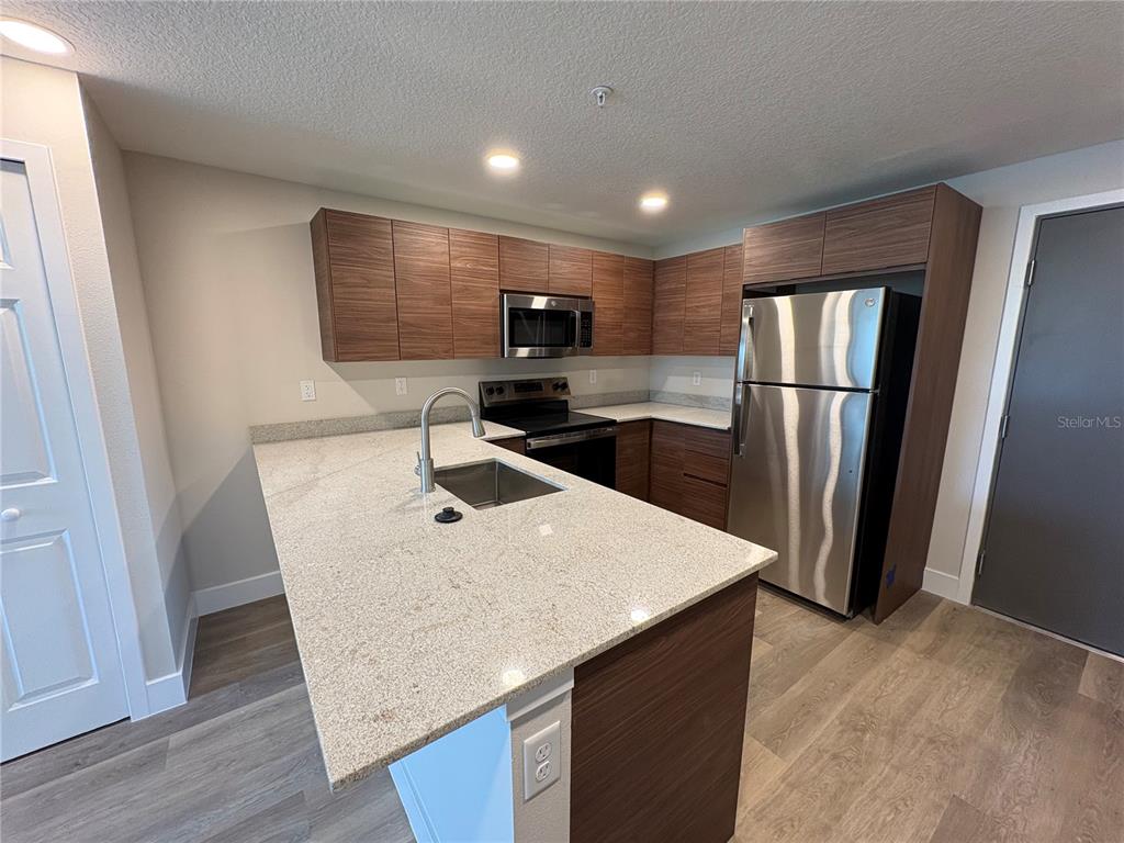 A kitchen features wood-grain cabinets, granite countertops, stainless steel appliances, and a central island — 4424 S TEXAS AVENUE UNIT 1-112, ORLANDO, FL