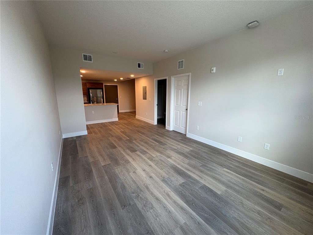 An open-concept living area features light-colored walls, wood-look flooring, and a kitchen in the background — 4424 S TEXAS AVENUE UNIT 1-112, ORLANDO, FL