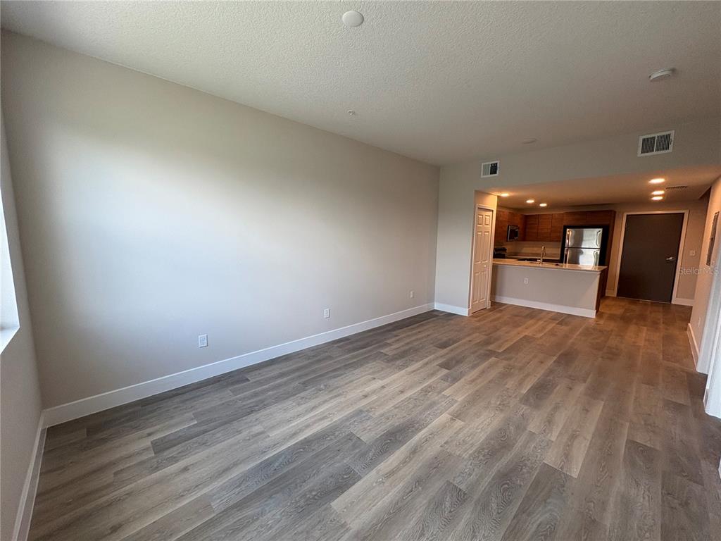 An open-concept living area features light-colored walls, wood-look flooring, and an adjacent kitchen — 4424 S TEXAS AVENUE UNIT 1-112, ORLANDO, FL