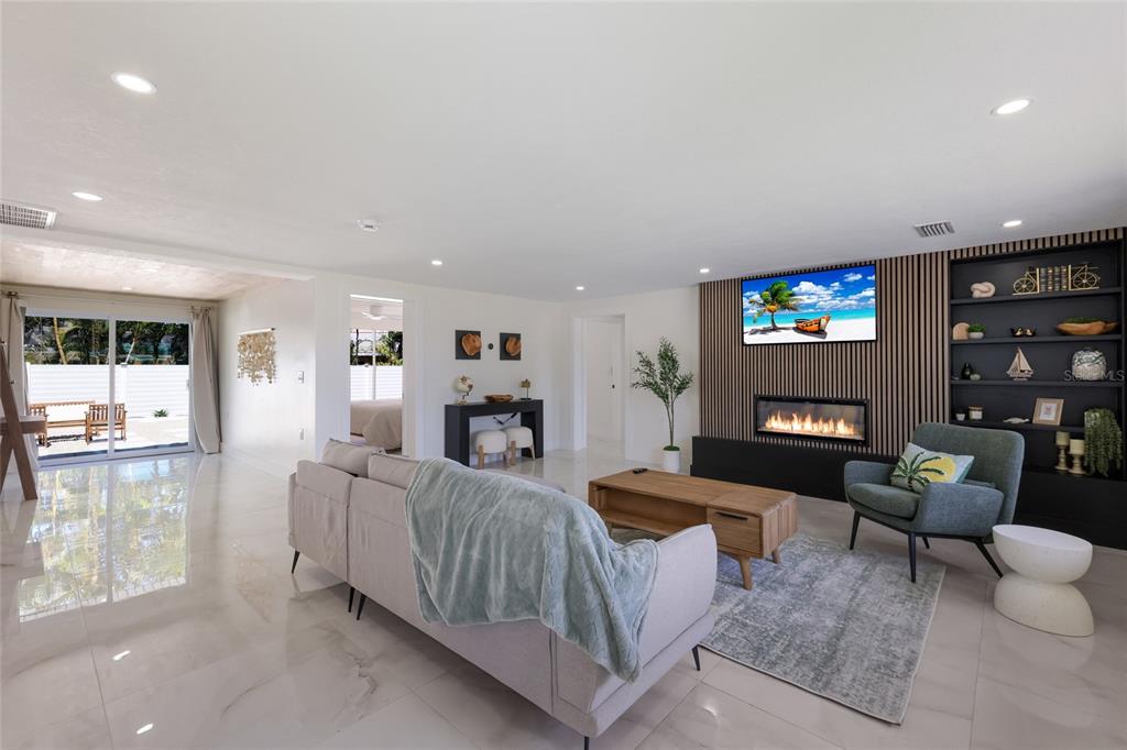 A modern living room features a fireplace, built-in shelving, a sofa, and sliding glass doors — 214 85TH STREET, HOLMES BEACH, FL