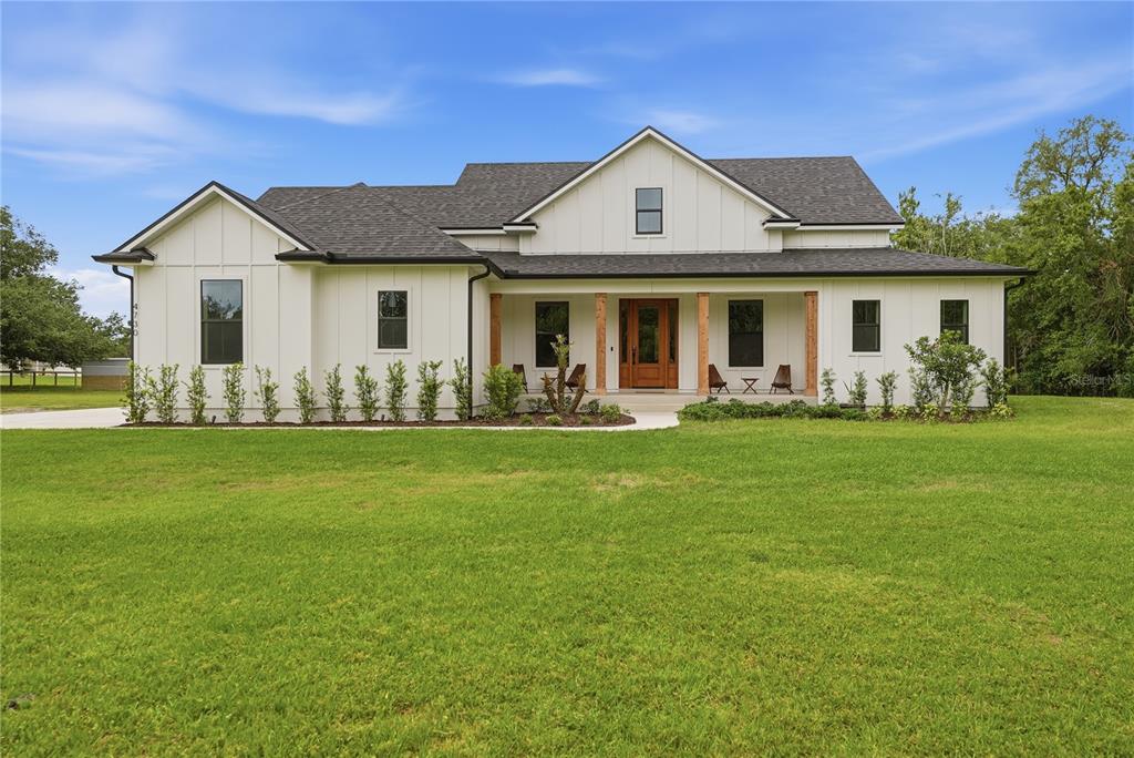 A white farmhouse with a dark roof and wooden porch columns sits on a lawn — 4730 QUAIL ROOST ROAD, ST CLOUD, FL