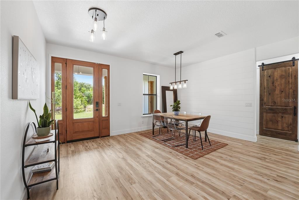 A dining room features wood-look flooring, a shiplap wall, a wooden table, and a barn door — 4730 QUAIL ROOST ROAD, ST CLOUD, FL