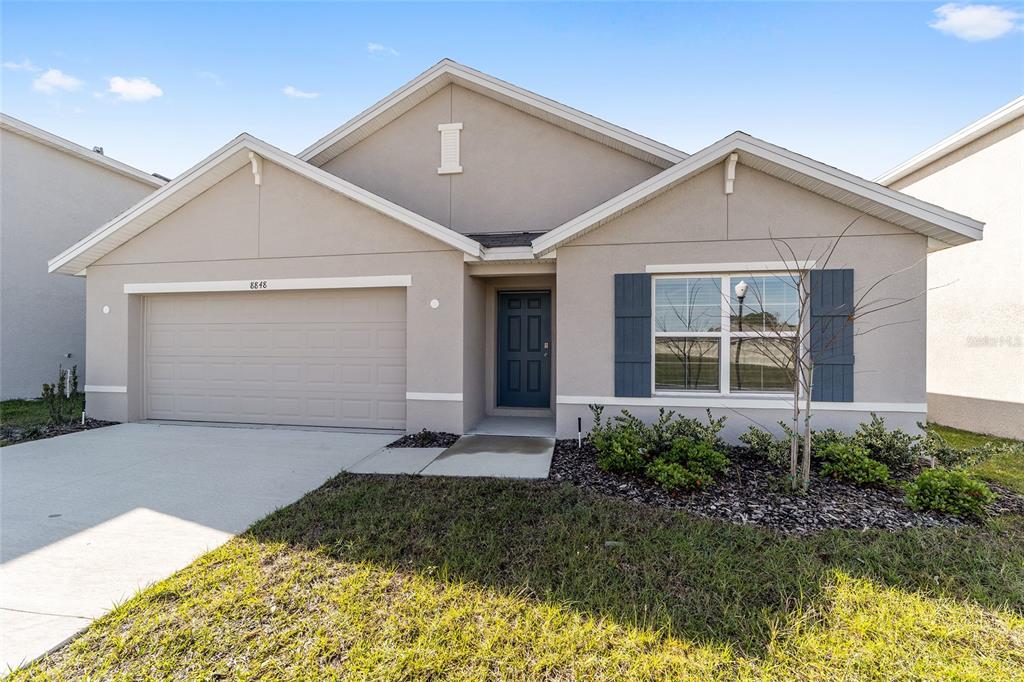 A single-story house with a beige stucco exterior, a two-car garage, and dark blue shutters — 8856 SW 49TH CIRCLE, OCALA, FL