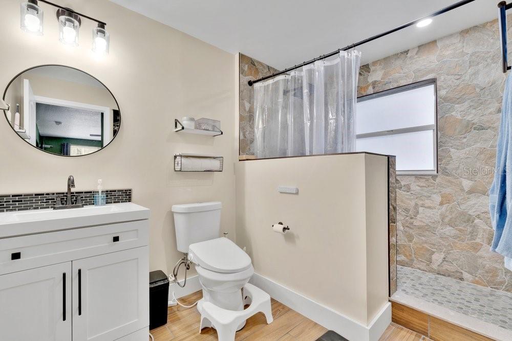 A bathroom featuring a white vanity, a toilet with a step stool, and a stone-tiled shower — 851 E UNIVERSITY AVENUE, ORANGE CITY, FL