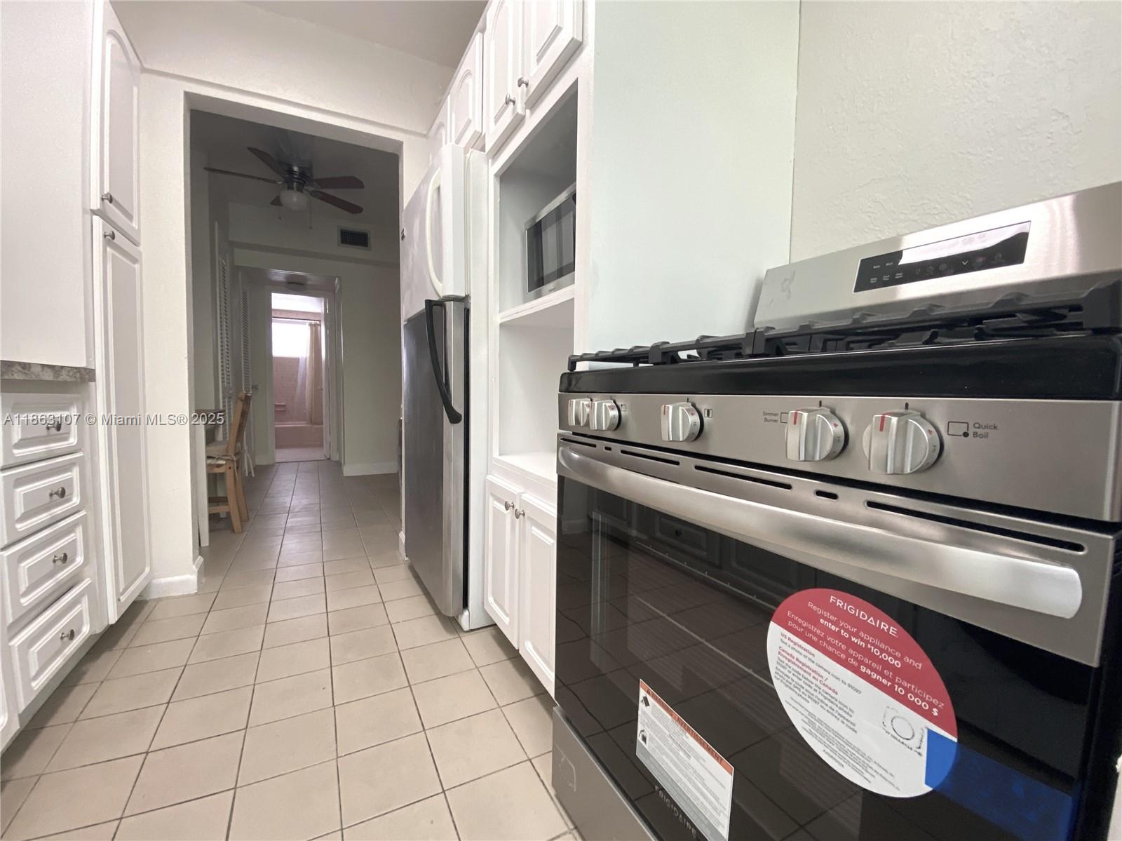 A kitchen features white cabinets, stainless steel appliances, and tile flooring leading to a hallway — 932 Euclid Ave # 2, Miami Beach FL 33139, MIAMI BEACH, FL
