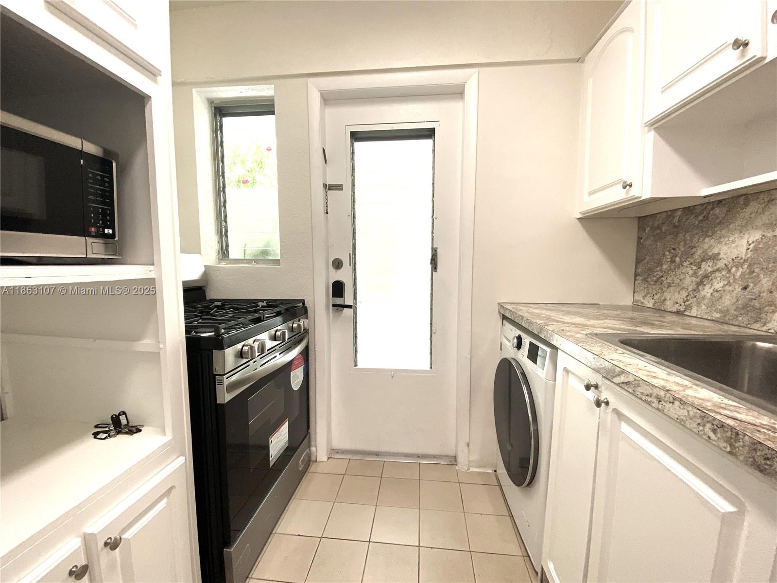 A small kitchen features white cabinets, a gas stove, a built-in washer, and tile flooring — 932 Euclid Ave # 2, Miami Beach FL 33139, MIAMI BEACH, FL