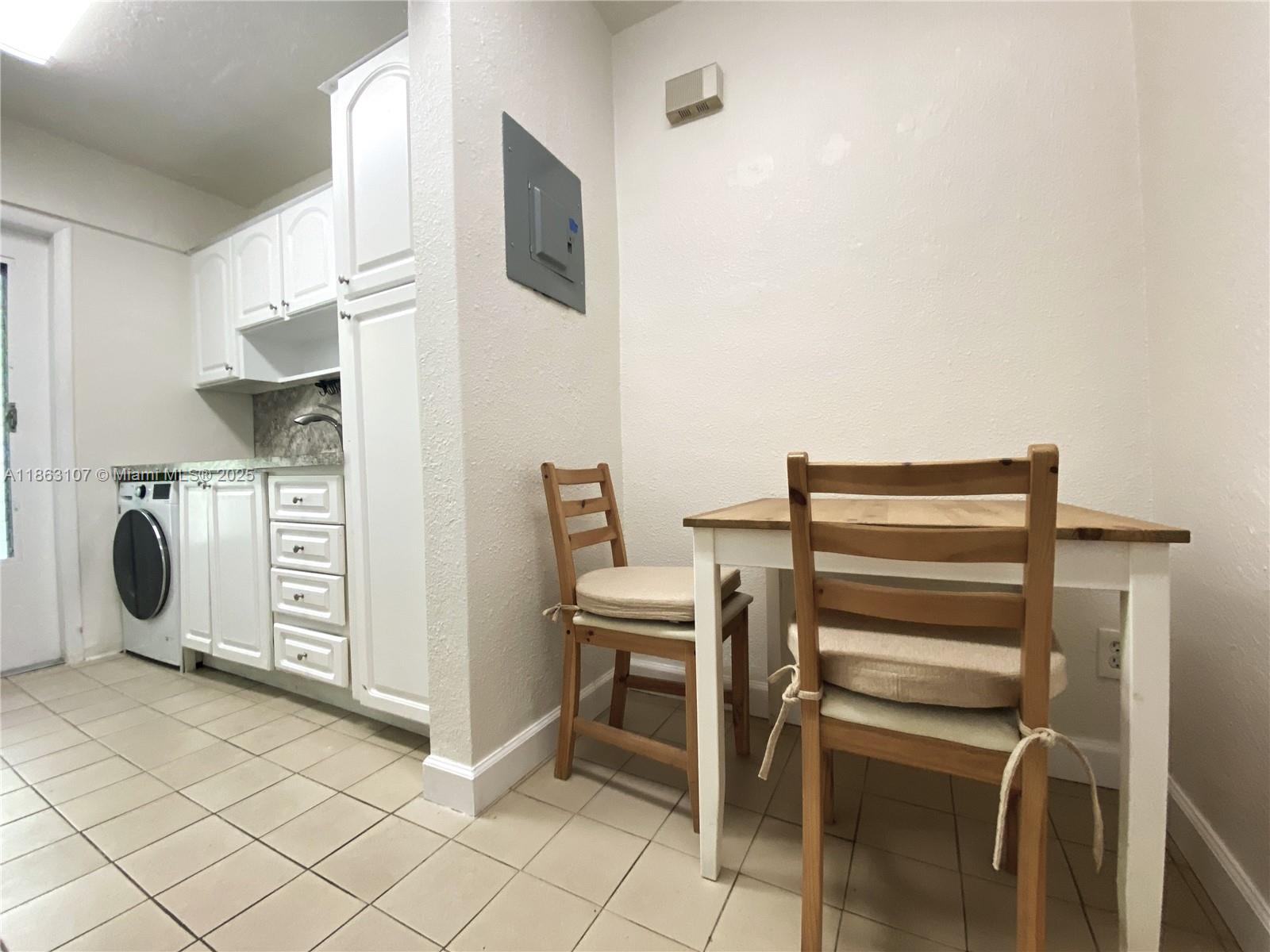 A small kitchen features white cabinets, a front-loading washer, and a wooden dining table — 932 Euclid Ave # 2, Miami Beach FL 33139, MIAMI BEACH, FL