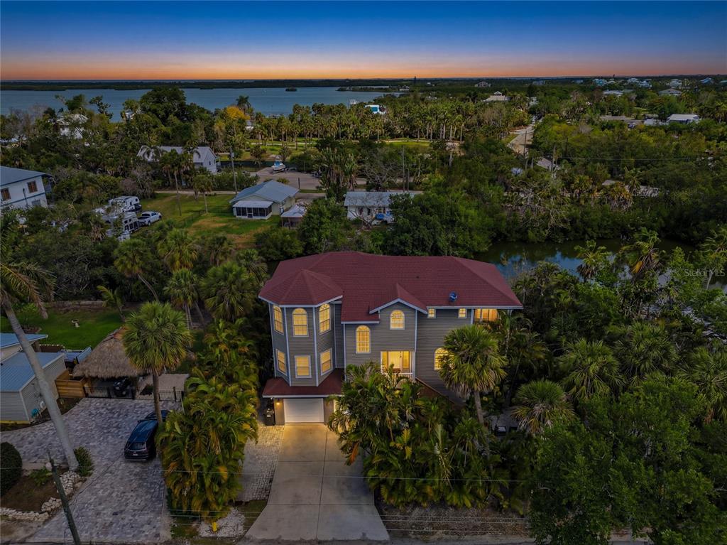 An aerial view shows a multi-story gray house with a red roof near water — 28 MICHIANA DRIVE, TERRA CEIA, FL
