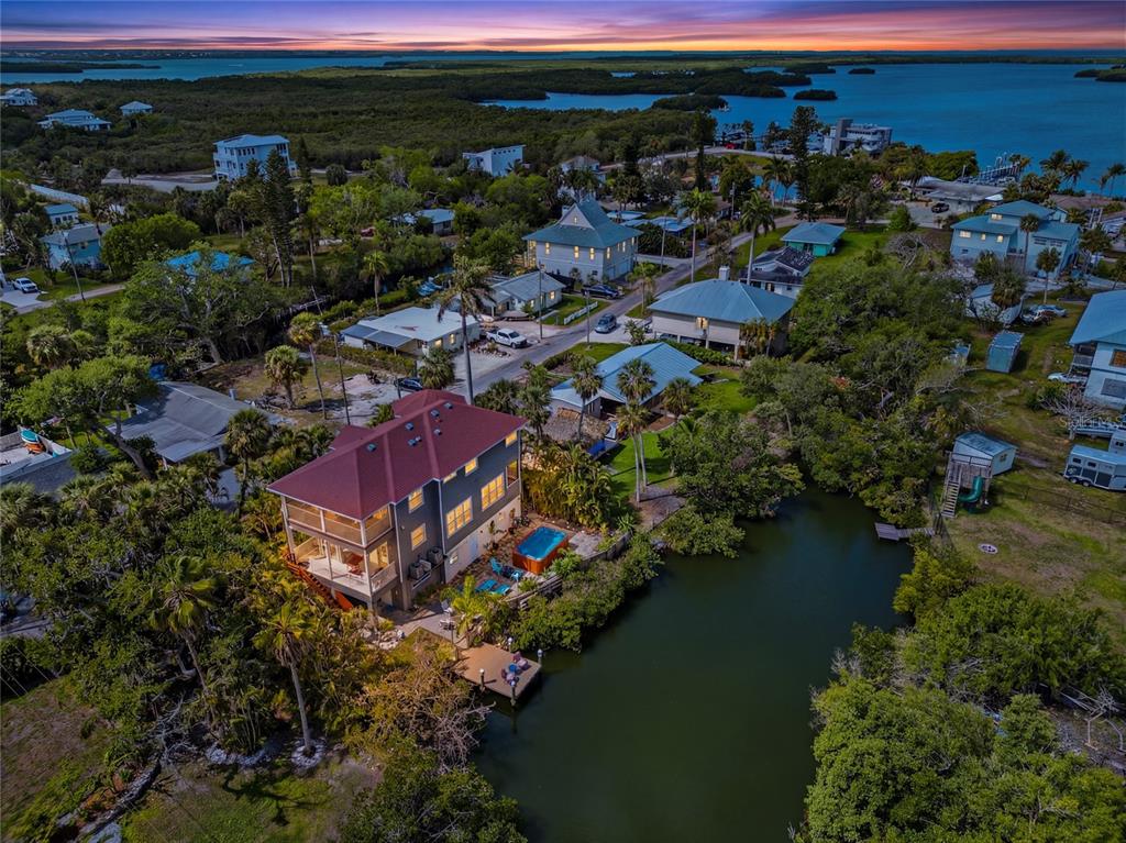 An aerial view shows a multi-story house with a red roof, pool, and private dock — 28 MICHIANA DRIVE, TERRA CEIA, FL