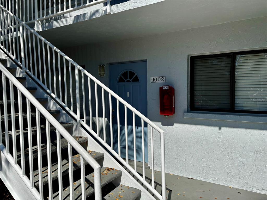 An exterior view of a building entrance with stairs, a blue door, and a fire extinguisher — 5310 26TH STREET W UNIT 1002, BRADENTON, FL