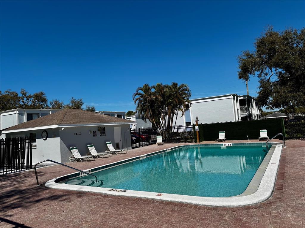 An outdoor swimming pool with a surrounding patio and a small building under a clear sky — 5310 26TH STREET W UNIT 1002, BRADENTON, FL