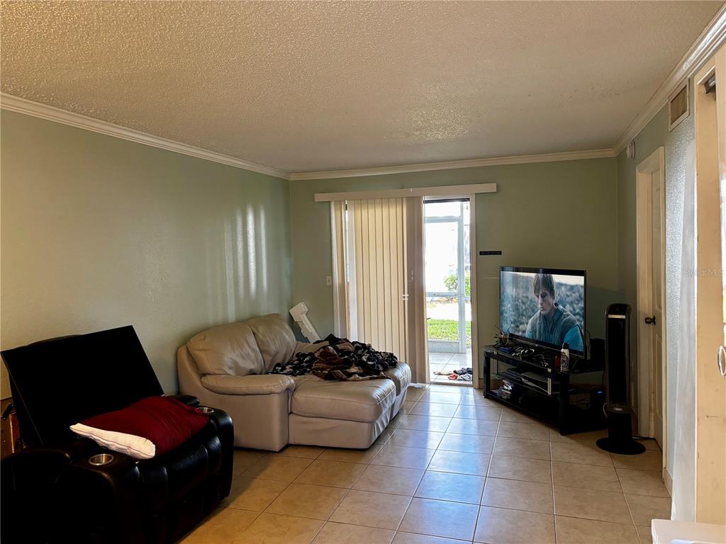 A living room features light green walls, tile flooring, a sliding glass door, and furniture — 5310 26TH STREET W UNIT 1002, BRADENTON, FL