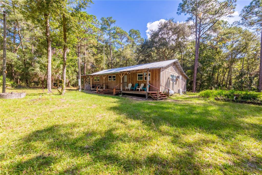 A rustic wooden cabin with a metal roof sits in a grassy, tree-filled yard — 6550 SW 100TH COURT, CEDAR KEY, FL, FL