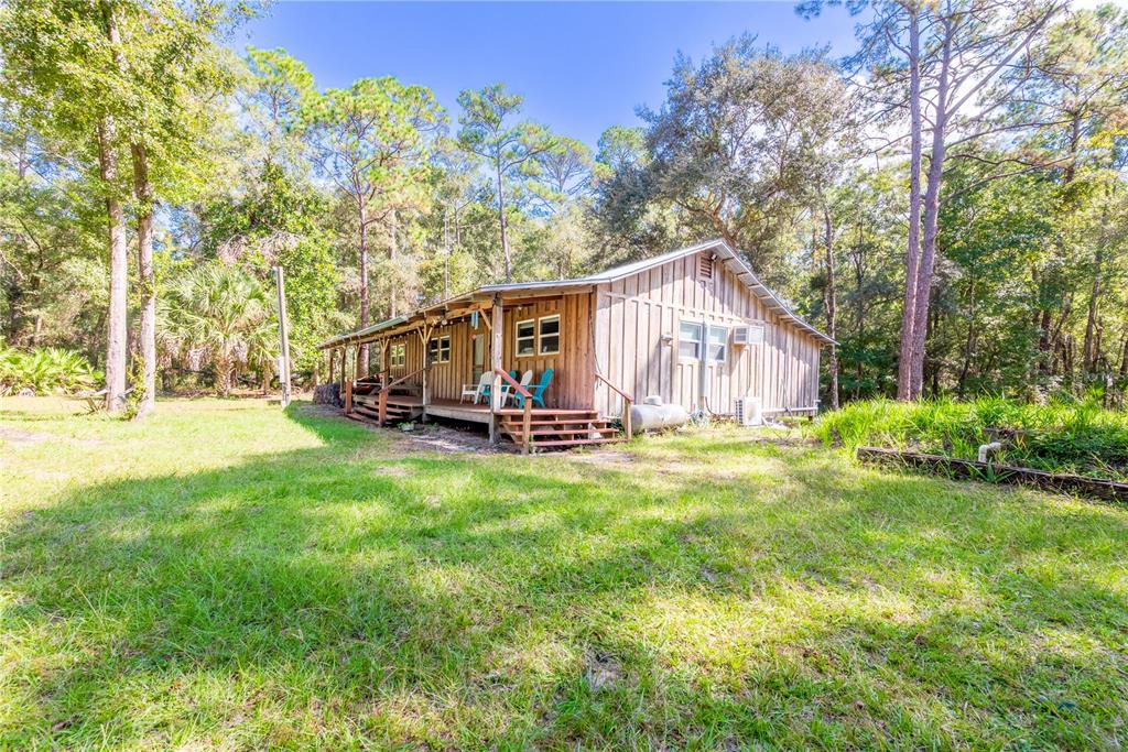 A wooden cabin with a covered porch sits in a grassy clearing surrounded by trees — 6550 SW 100TH COURT, CEDAR KEY, FL, FL