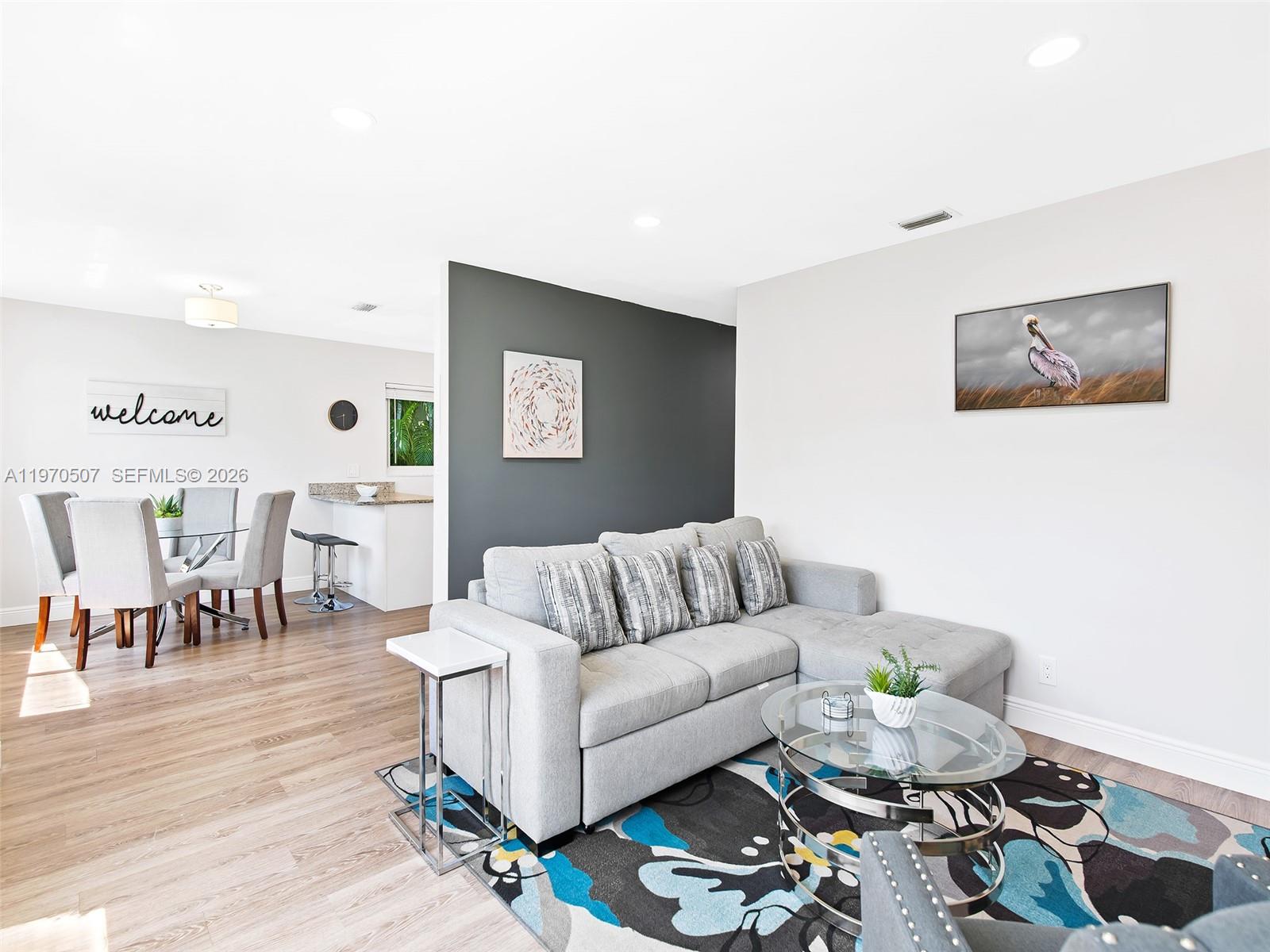 A living room with a gray sectional sofa, glass coffee table, and adjacent dining area — 3405 Norfolk St, Pompano Beach FL 33062, POMPANO BEACH, FL