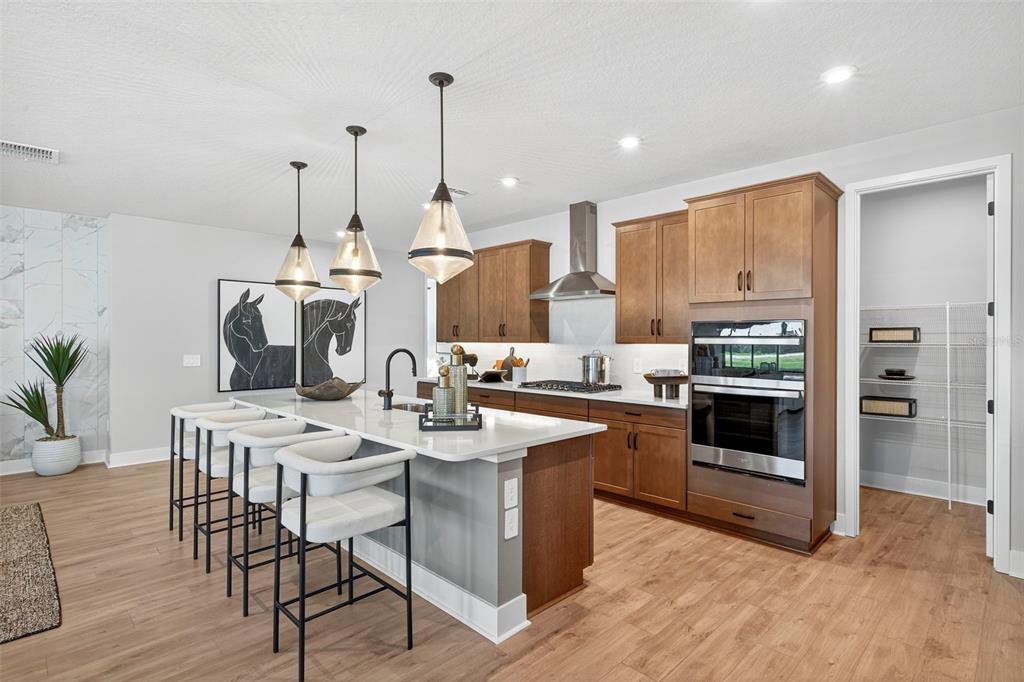 A modern kitchen features wood cabinets, a white quartz island with bar seating, and stainless appliances — 34725 FLOWER PATCH DRIVE, DADE CITY, FL