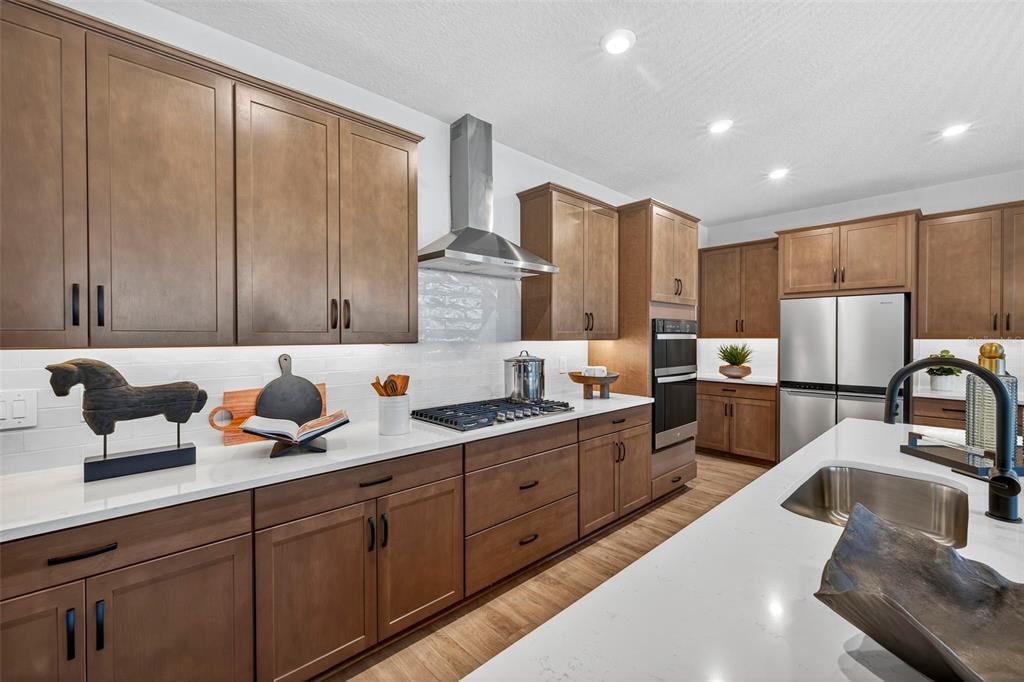 A modern kitchen features wood cabinets, white countertops, stainless steel appliances, and a central island — 34725 FLOWER PATCH DRIVE, DADE CITY, FL