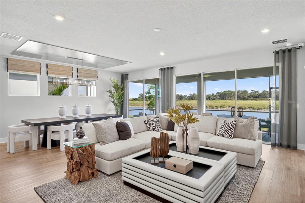 A modern living and dining area features a large sectional sofa, wood-base table, and water views — 34725 FLOWER PATCH DRIVE, DADE CITY, FL